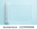 Roll of transparent polyethylene food film for packing products on the pastel blue table. Empty place for text or objects. Top view.