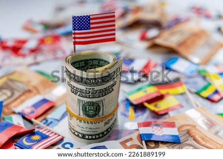 A roll of US dollars with the American flag on top of a other currencies and country flags. Dollar hegemony concept.
