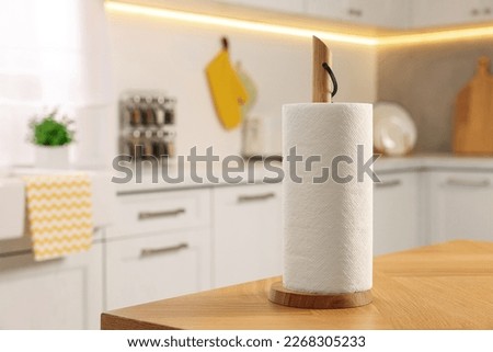 Roll of white paper towels on wooden table in kitchen, space for text