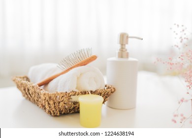 Roll Up Of White Towels And Comp On Basket, Ceramic Soap, Shampoo Bottles On White Table With Copy Space On Blurred Living Room Background. For Product Display Montage.