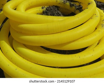 a roll of yellow plastic pipe laying on a muddy sidewalk