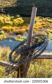 Rolled Up Barb Wire Fencing Hanging On Fence Post In Colorful Mountain Meadow