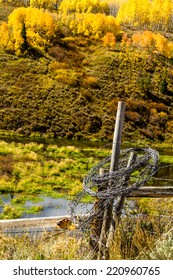 Rolled Up Barb Wire Fencing Hanging On Fence Post In Colorful Mountain Meadow