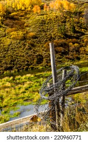 Rolled Up Barb Wire Fencing Hanging On Fence Post In Colorful Mountain Meadow