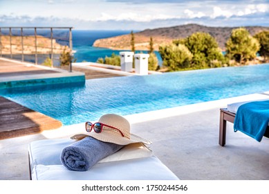 Rolled Beach Towel, Sunglasses On The Hat Lying On The Chaise-longue / Sunbed Overlooking Pool,  Panoramic Sea And Mountaing View