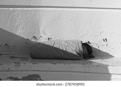 Rolled bedding and a cap sit on a worn concrete ledge, suggesting homelessness in Long Beach.
