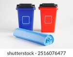 Rolled blue polyethylene garbage bags near two plastic waste bins or containers. White background. Separate waste collection. Household cleaning products. Photo. Selective focus. Copy space. Close-up
