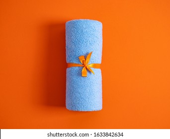 Rolled Blue Terry Towel Tie Up By Orange Ribbon Against A Orange Background.Top View.