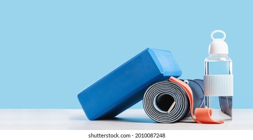 Rolled blue yoga mat. Yoga block water bottle and red rubber band. Gender neutral fitness exercise concept. copy space. Active lifestyle sport. Workout at home or gym web banner - Powered by Shutterstock