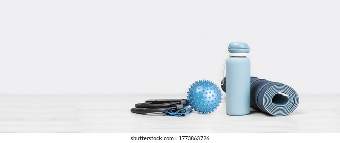 Rolled blue yoga mat. exercise resistance band water bottle on grey wooden surface. Gender neutral fitness and exercise concept with copy space. Active lifestyle. Workout at home or gym web banner - Powered by Shutterstock