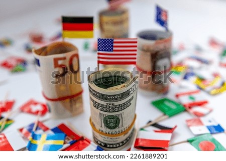 Rolled bundles of major currencies and country flags with the US Dollar and American flag in front. Dollar hegemony concept.