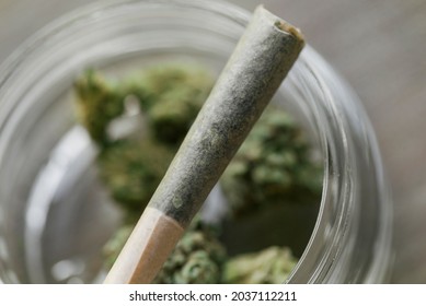 Rolled cigarette with legal recreational weed resting on jar filled with flower. Macro close up with focus on joint.