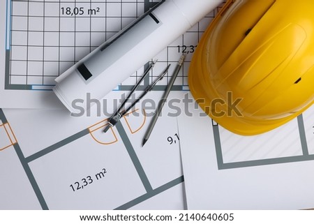 Rolled construction drawing, safety hat, pair of compasses and pencil on house plan, flat lay