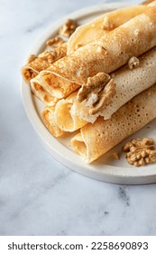 Rolled crepes or thin pancakes with honey and nuts on a white marble background close up, text space. Maslenitsa or Pancake day traditional food concept. Vertical - Shutterstock ID 2258690893