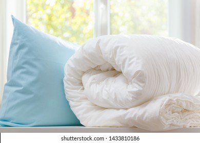 A Rolled Duvet And Pillow Lie On A Dresser Against The Background Of A Blurred Window. Household.