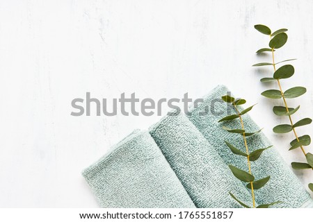 Rolled fluffy green towels and green eucalyptus branch on white background. Minimalist scandinavian style. Hygiene, wellness well-being, body care concept. Copy space, flat lay