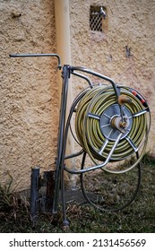 A Rolled Up Garden Hose On A Yellow House Wall.