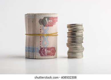 Rolled Hundred dirham bills placed along with stack of coins on white background. Return on investment- a concept.