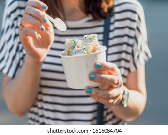 Rolled ice cream in cone cup in woman hands. Woman in striped dress holds cone cup with thai style kiwi banana rolled ice cream.