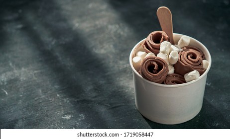 Rolled ice cream with in cone cup on dark rustic background. Iced rolls with chocolate. Thai style chocolate rolled ice cream with copy space for text or design. Banner. Natural hard daylight