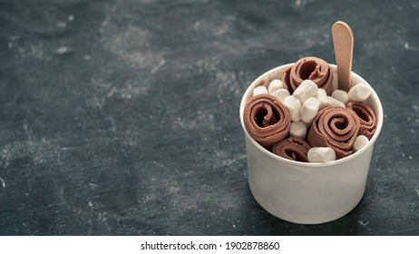 Rolled ice cream with in cone cup on dark rustic background. Iced rolls with chocolate. Thai style chocolate rolled ice cream with copy space for text or design. Banner. Natural daylight