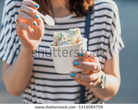 Rolled ice cream in cone cup in woman hands. Woman in striped dress holds cone cup with thai style kiwi banana rolled ice cream.