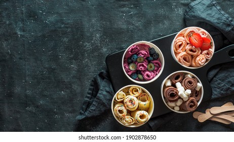 Rolled ice cream in cone cups on dark background. Different iced rolls top view or flat lay. Thai style rolled ice cream with copy space in center for text or design. Banner