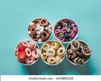 Rolled ice creams in cone cups on blue background. Different iced rolls, top view or flat lay. Thai style rolled ice cream