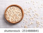 Rolled oat flakes, rolled oats in a wooden bowl on linen. Husked and steamed oat groats rolled into flakes and lightly toasted. Whole-grain food from husked common oats, Avena sativa, a cereal grain.