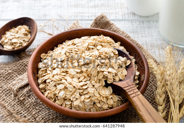 Rolled oats or oat flakes in bowl with wooden\
spoons, golden wheat ears and bottle of milk on background. Healthy\
lifestyle, healthy eating\
concept
