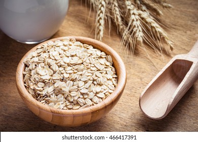 Rolled oats (oat flakes), milk and golden wheat ears on wooden background. Raw food ingredients, healthy lifestyle, cooking food, healthy food concept