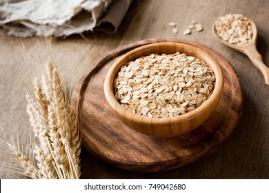 Rolled oats, organic oat flakes in wooden bowl and golden wheat ears on wooden background. Healthy lifestyle, healthy eating, vegan food concept