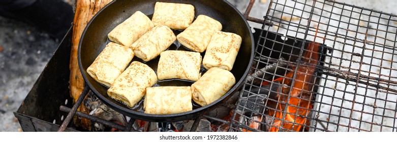 rolled pancakes with filling are fried in a frying pan on the fire in the grill. winter cooking food in nature outdoor. traditional national russian folk dish for the celebration of maslenitsa. banner