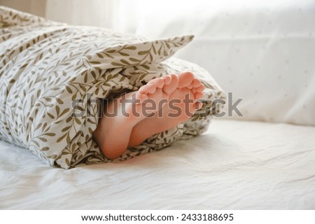 Rolled person. A child wrapped in a blanket with sticking out feet lies on the bed in the bedroom. Sunny morning dream. Psychology comfort. Toes up. Close-up. High quality.