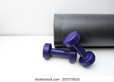 Rolled Up Rubber Yoga Mat, Two Purple Dumbbells On A White Background. Fitness And Sport Concept. Active Lifestyle, Place For Text.