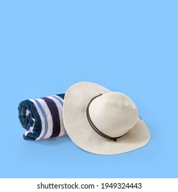 Rolled Striped Beach Towel And Large White Brim Hat With A Light Blue Background