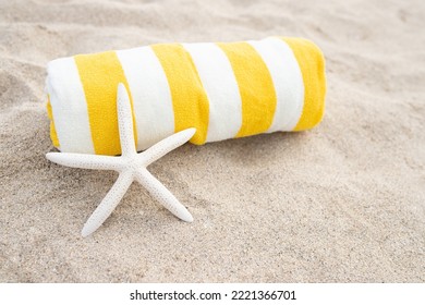 Rolled up striped white and yellow towel, white starfish shell on the sandy beach. Sunny day. The concept of tanning, vacation, relaxation, retreat, vacation, travel, sunbathing. Copy space. - Shutterstock ID 2221366701
