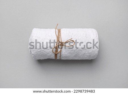 Rolled white towel tied with a rope on gray paper background.