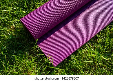 Rolled Yoga Mat On Green Grass In Summer, Close Up And Top View. Fitness Concept