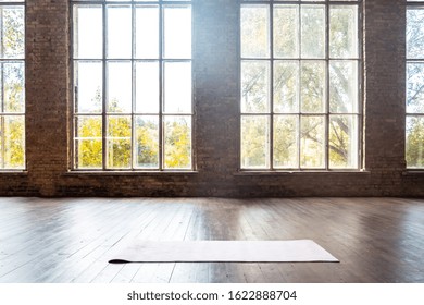 Rolled yoga pilates rubber mat inside gym studio on wooden floor sport workout fitness club class training exercise equipment in clean room interior space bid windows nobody background concept.