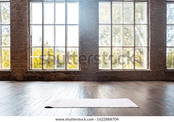 Rolled yoga pilates rubber mat inside gym studio\
on wooden floor sport workout fitness club class training exercise\
equipment in clean room interior space bid windows nobody\
background concept.