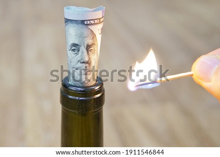 A rolled-up one hundred American dollar bill sticks out of a red wine bottle.