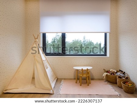Roller blinds in the children's room. Automatic roller shades on the window in the interior of child's room. Trees outside. Electric sunscreen curtains for home. Playhouse and toys are there.