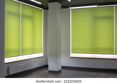 Roller blinds closeup on the window in the interior. Roller shades for big windows. Automated curtains for office. Green color, monochrome material. Window coverings.