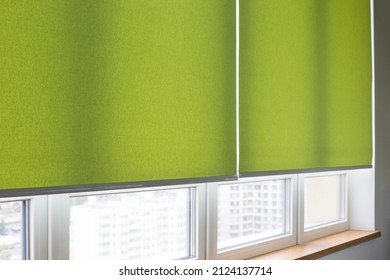 Roller blinds closeup on the window in the interior. Roller shades for big windows. Electric curtains for office. Green color, monochrome material. Window coverings.