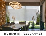 Roller blinds in the interior. Automatic solar shades large size on the window. Modern interior with wood decor panel on the wall. Green plants in hi-tech flower pots. Electric curtains for home. 