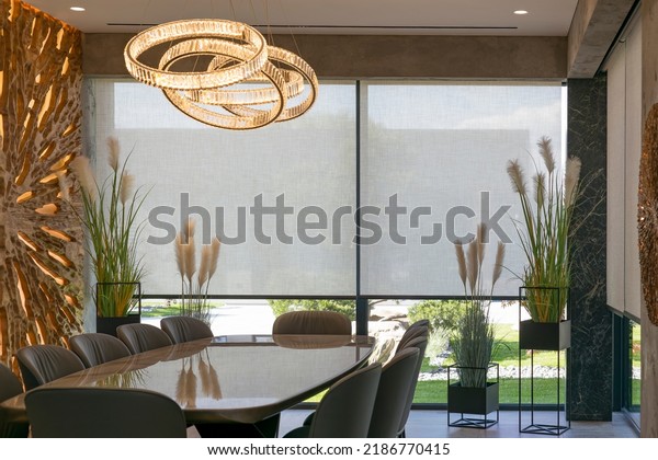 Roller blinds in the interior. Automatic solar shades\
large size on the window. Modern interior with wood decor panel on\
the wall. Green plants in hi-tech flower pots. Electric curtains\
for home. 