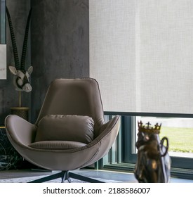 Roller blinds of large sizes on the window in the interior. Automatic solar shades, fabric with linen texture. In front of a large window is a chair on a carpet. Outside is a view of the garden. - Shutterstock ID 2188586007