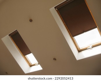 Roller blinds on roof windows close up in the interior. Roller shades for skylights. Brown color.
