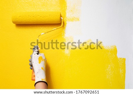 Roller Brush Painting, Worker on surface wall apartment, renovating with yellow color  paint. Leave empty copy space white to write descriptive text beside.